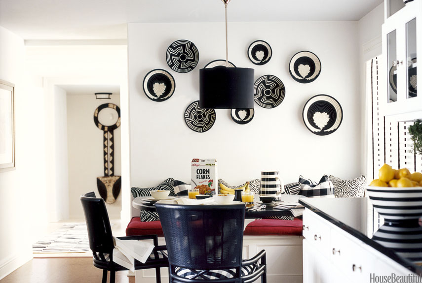 Designer Carleton Varney created a "young and snappy" kitchen in a 1929 Wisconsin cottage by using a black-and-white color scheme. Walls painted Benjamin Moore's Decorator's White set off by Unity and Embrace baskets made in Rwanda, from macys.com. The table was made by H.J. Martin and Son, the nationwide interior contracting company owned by the homeowners, Edward and Terri Martin. Catalina chairs from Ficks Reed. Through the doorway is an African wall-hanging from Hemingway Gallery. Striped bowl and pitcher, Crate &amp; Barrel. 